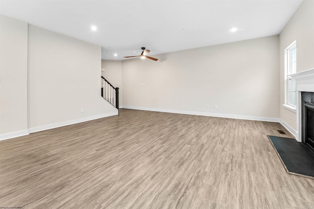 unfurnished living room with recessed lighting, a fireplace with flush hearth, wood finished floors, baseboards, and stairs