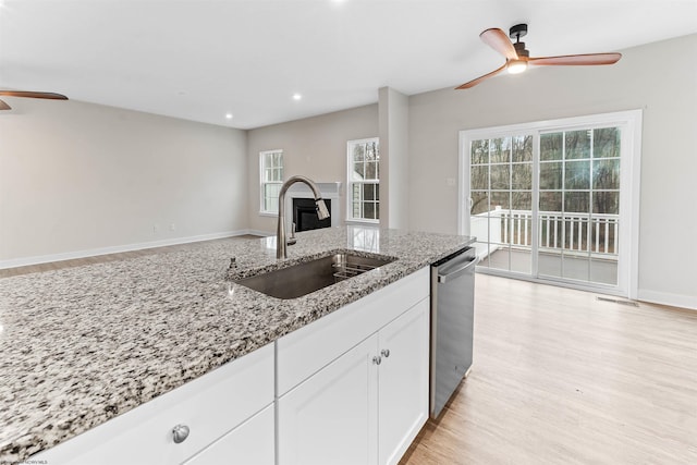 kitchen with light wood finished floors, white cabinets, a sink, light stone countertops, and dishwasher