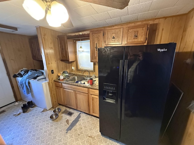 kitchen with a sink, wood walls, brown cabinetry, and black fridge