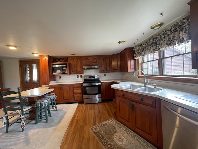 kitchen with stainless steel appliances, light countertops, light wood-style floors, a sink, and under cabinet range hood