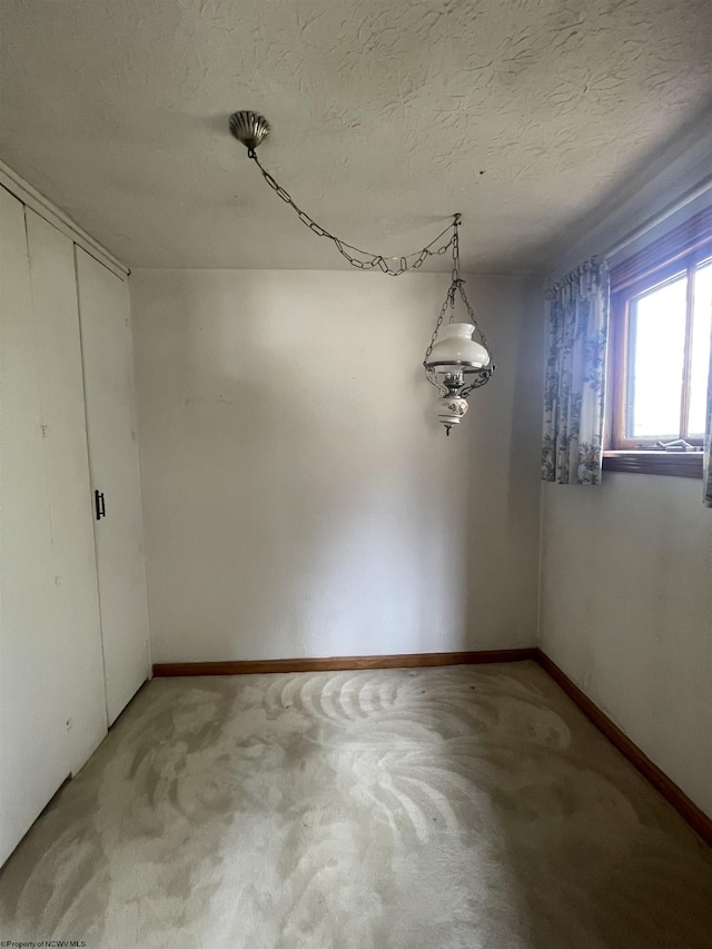 unfurnished dining area with a textured ceiling, carpet floors, and baseboards