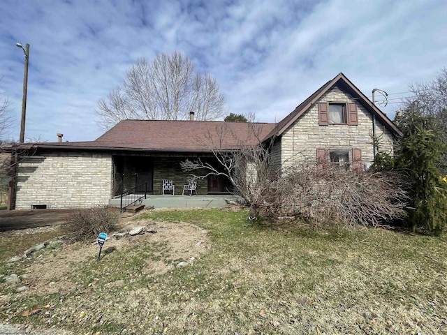 back of property featuring stone siding and a lawn