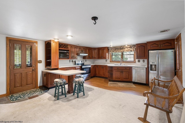 kitchen with under cabinet range hood, a peninsula, a sink, light countertops, and appliances with stainless steel finishes