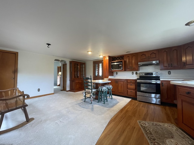 kitchen featuring arched walkways, light countertops, stainless steel range with electric stovetop, built in microwave, and under cabinet range hood