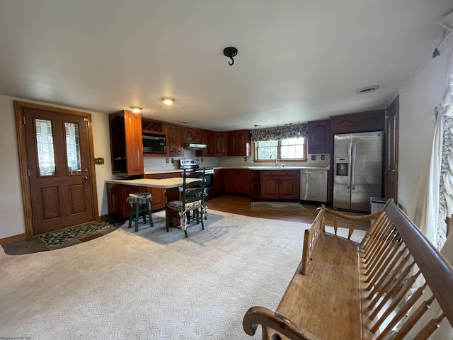 kitchen with baseboards, a peninsula, stainless steel appliances, light countertops, and under cabinet range hood