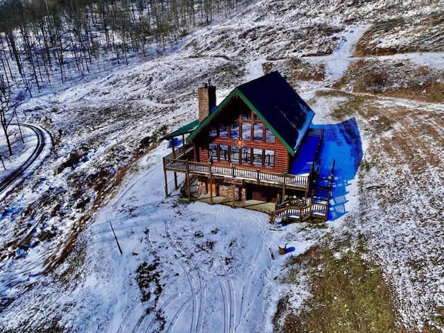 snow covered house with a chimney, a deck, and log veneer siding