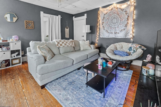 living room with a drop ceiling, wood-type flooring, and baseboards