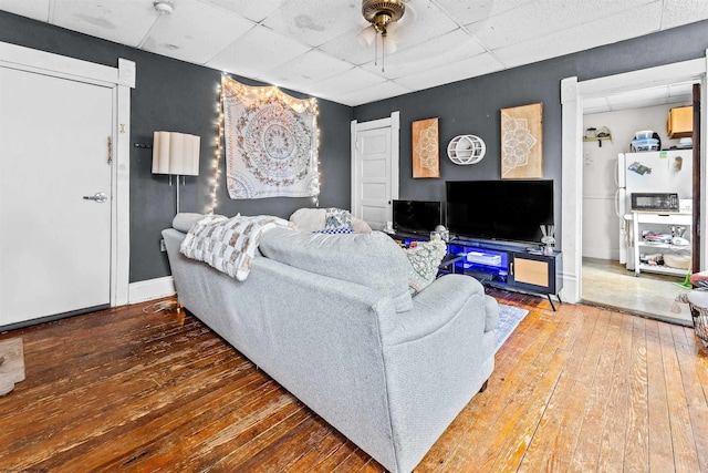 living area featuring hardwood / wood-style floors, a drop ceiling, and baseboards