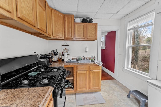 kitchen featuring baseboards, black range with gas stovetop, light countertops, a paneled ceiling, and a sink