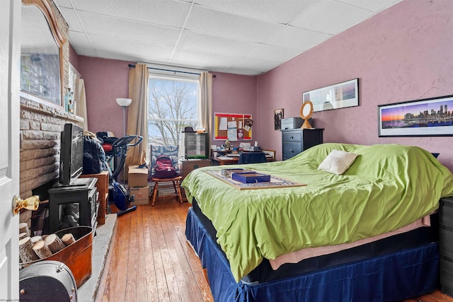 bedroom featuring a textured wall, a paneled ceiling, wood-type flooring, and a wood stove