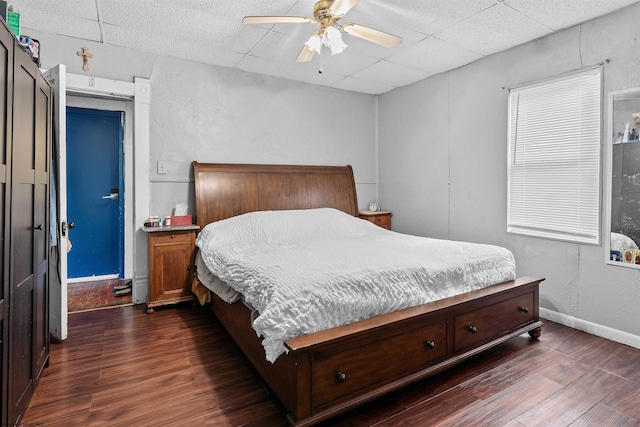 bedroom with a paneled ceiling, baseboards, dark wood finished floors, and a ceiling fan