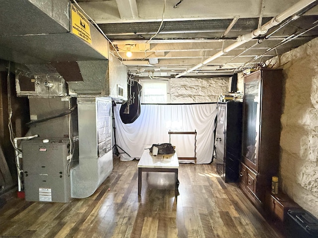 basement featuring visible vents, heating unit, and wood finished floors