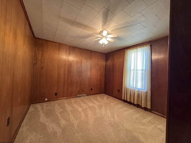 empty room featuring visible vents, light carpet, ceiling fan, wooden walls, and baseboards