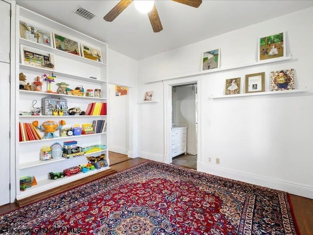 recreation room featuring baseboards, visible vents, a ceiling fan, and wood finished floors