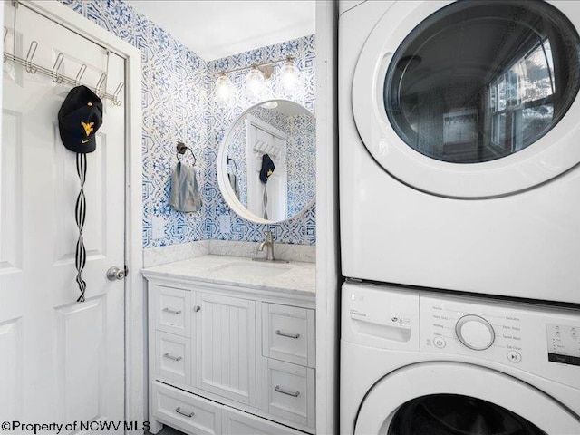 washroom featuring stacked washer and dryer, a sink, laundry area, and wallpapered walls