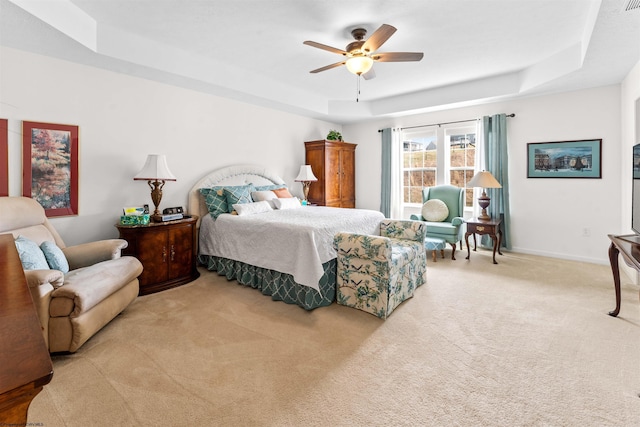 bedroom with a ceiling fan, a raised ceiling, light carpet, and baseboards