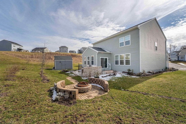 rear view of property featuring a fire pit, a lawn, an outdoor structure, a patio area, and a shed