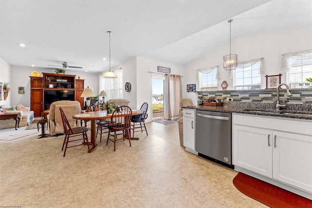 kitchen with a sink, white cabinets, stainless steel dishwasher, dark stone countertops, and plenty of natural light