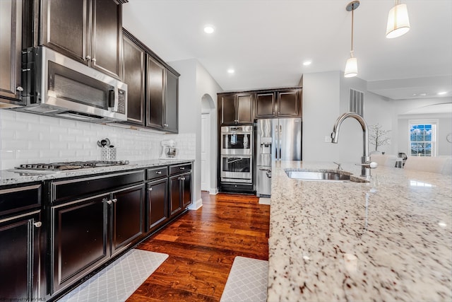 kitchen with arched walkways, dark wood-style floors, appliances with stainless steel finishes, light stone counters, and a sink