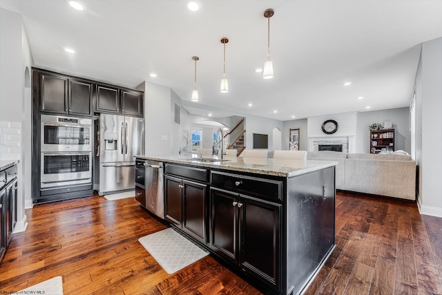 kitchen featuring dark wood-style flooring, a fireplace, appliances with stainless steel finishes, open floor plan, and a sink