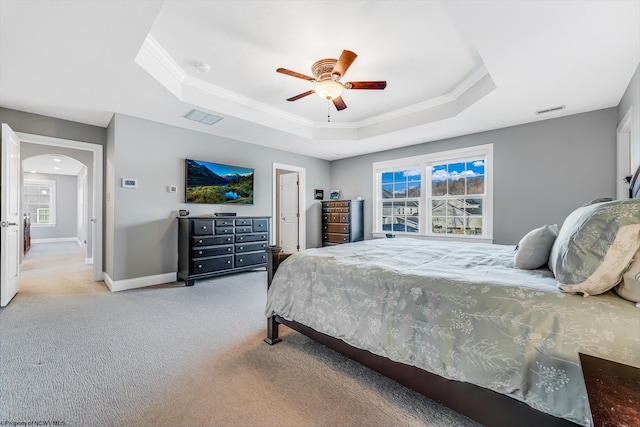 bedroom featuring multiple windows, a tray ceiling, arched walkways, and carpet flooring