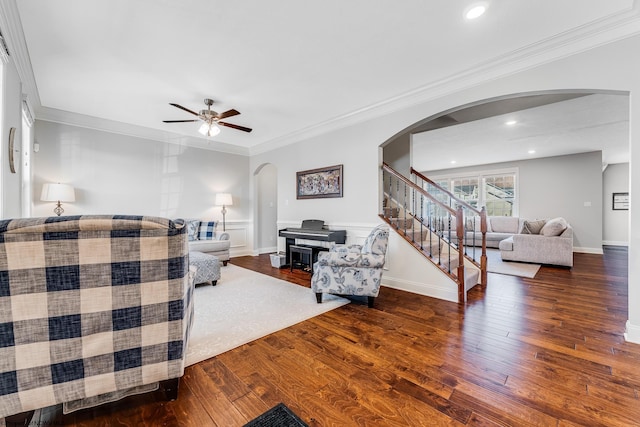 living area with arched walkways, stairway, ornamental molding, a ceiling fan, and wood finished floors