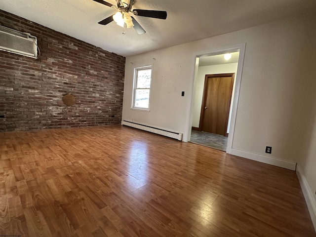 empty room featuring a wall unit AC, baseboard heating, brick wall, wood finished floors, and baseboards