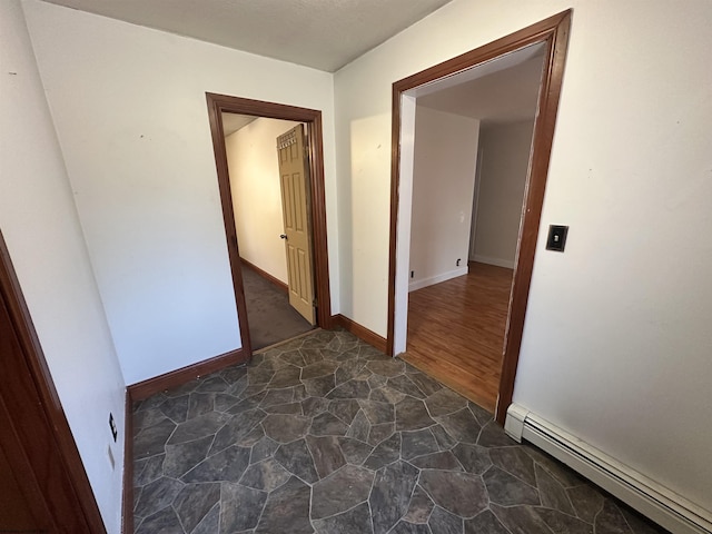 hallway with a baseboard heating unit, stone finish floor, and baseboards