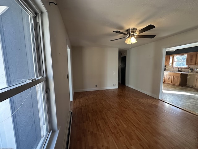 unfurnished room with ceiling fan, a textured ceiling, a sink, wood finished floors, and baseboards