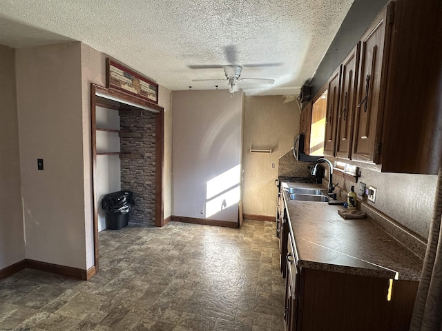 kitchen featuring a sink, a ceiling fan, baseboards, dark brown cabinets, and dark countertops