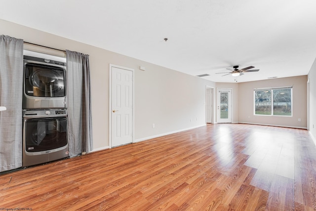 unfurnished living room featuring ceiling fan, stacked washer and dryer, visible vents, baseboards, and light wood-type flooring