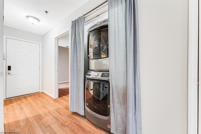 laundry area featuring baseboards, laundry area, stacked washing maching and dryer, and light wood-style floors