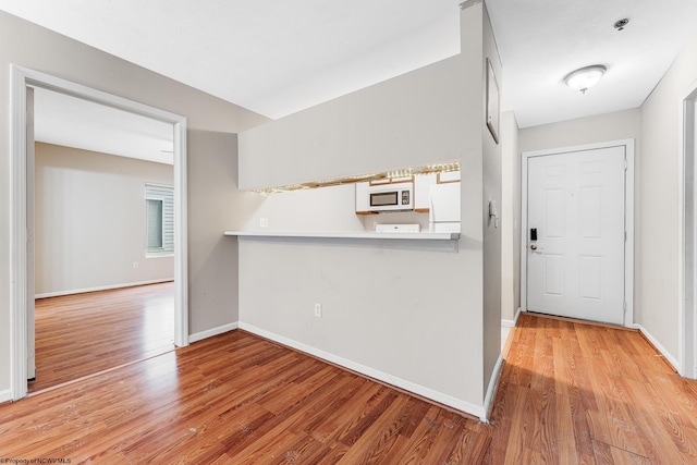 kitchen featuring light wood-style flooring, a peninsula, white appliances, baseboards, and light countertops