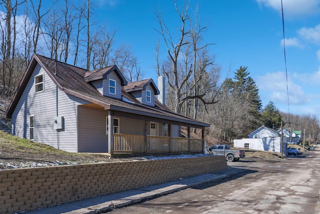 view of side of home with a shingled roof, covered porch, and a chimney