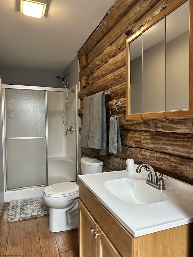 bathroom with rustic walls, a stall shower, toilet, wood finished floors, and vanity