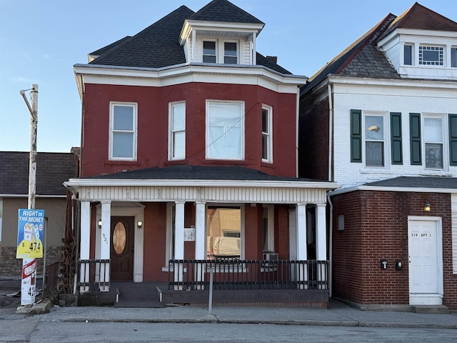 view of front of home with covered porch, brick siding, and roof with shingles