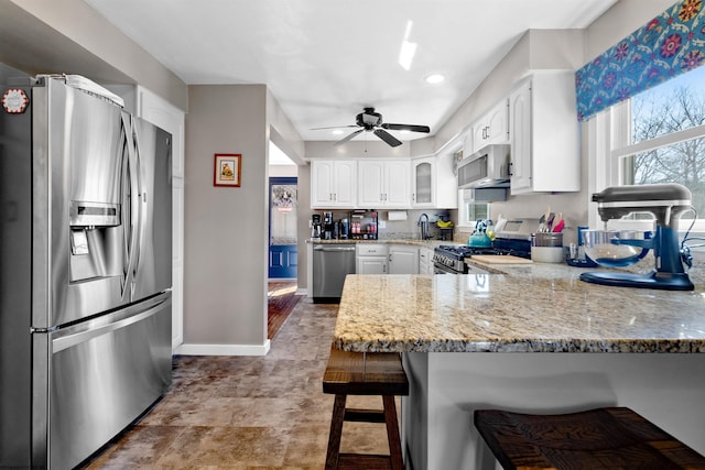 kitchen with appliances with stainless steel finishes, a breakfast bar, a peninsula, light stone countertops, and white cabinetry