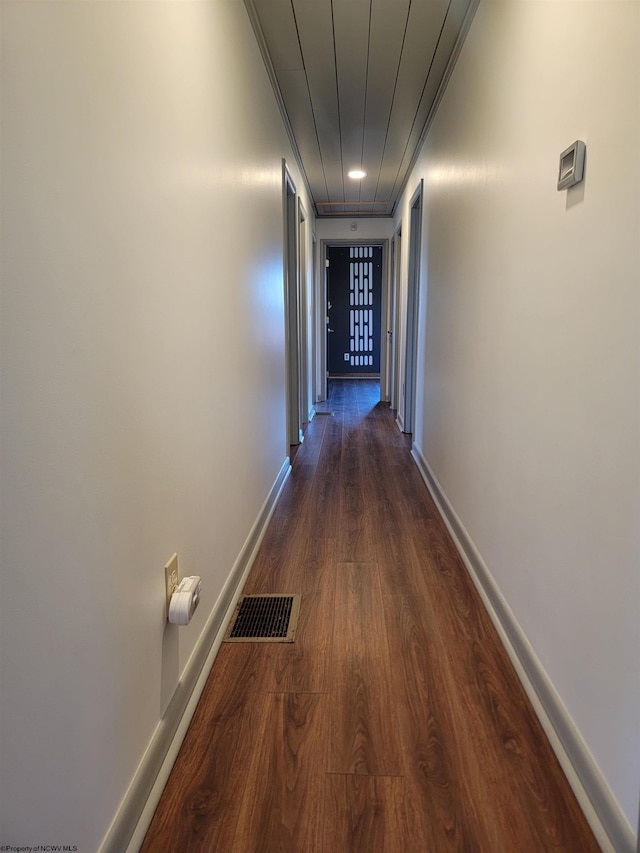 hall featuring dark wood-style flooring, visible vents, and baseboards