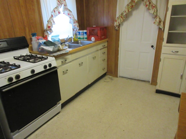 kitchen featuring white cabinets, white gas stove, wood walls, light floors, and a sink