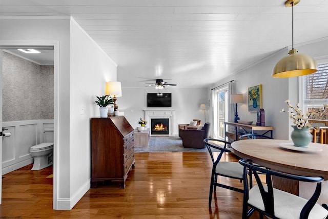 dining room with a wainscoted wall, a lit fireplace, ornamental molding, and wood finished floors