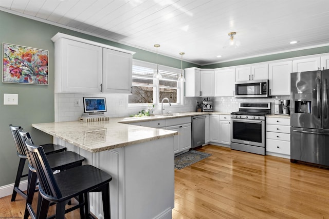 kitchen featuring stainless steel appliances, a peninsula, a sink, white cabinetry, and light wood-type flooring