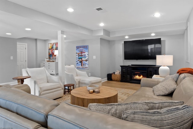 living area with visible vents, a glass covered fireplace, wood finished floors, and recessed lighting