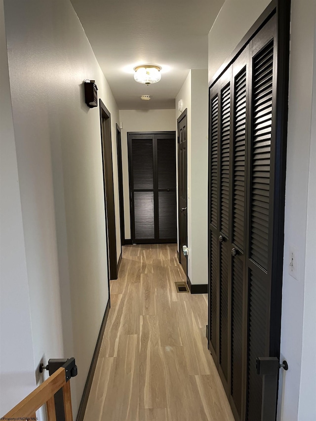 hall with light wood-style flooring, visible vents, and baseboards