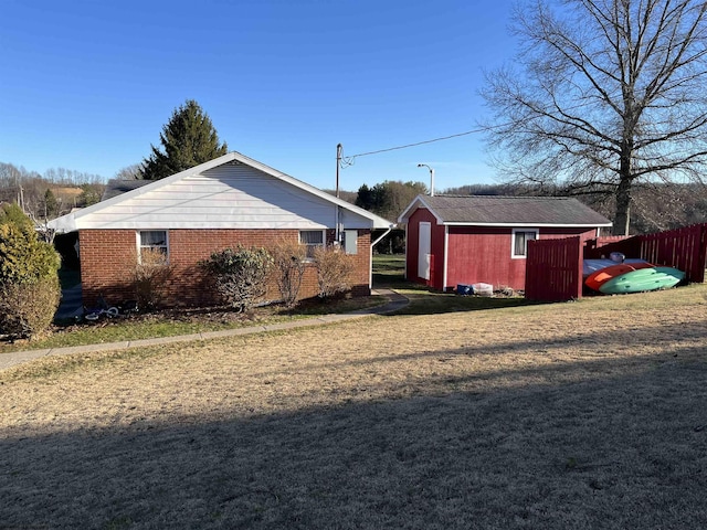 view of side of property featuring a lawn, an outbuilding, a storage unit, fence, and brick siding