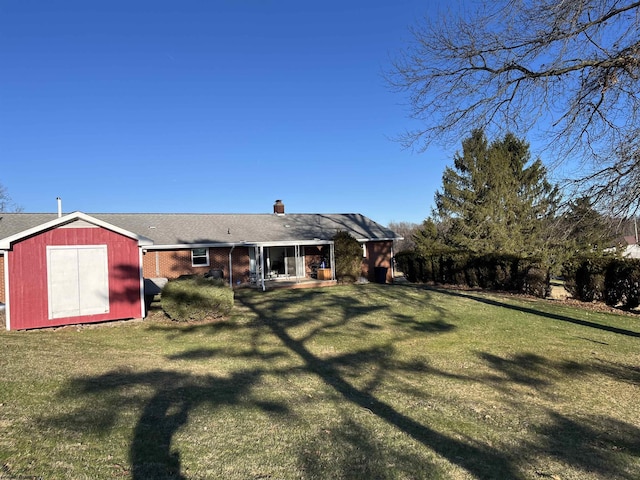 back of house with a storage shed, brick siding, an outdoor structure, a lawn, and a chimney