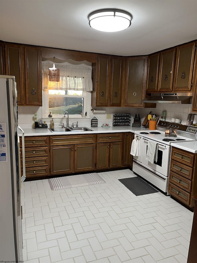 kitchen featuring white appliances, tasteful backsplash, under cabinet range hood, and a sink