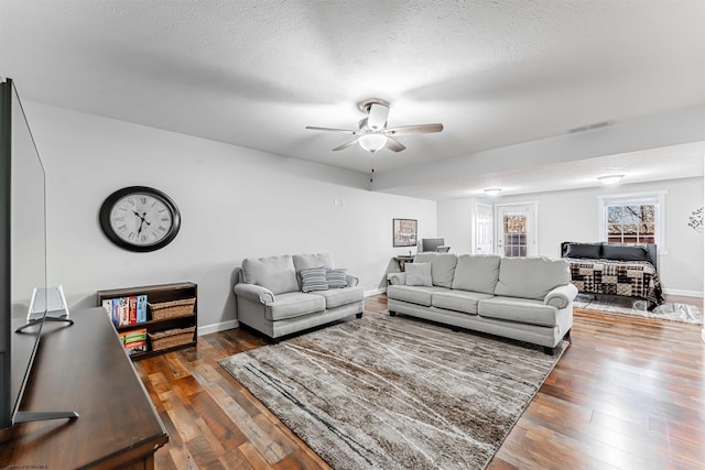 living area featuring a ceiling fan, wood-type flooring, visible vents, and a textured ceiling