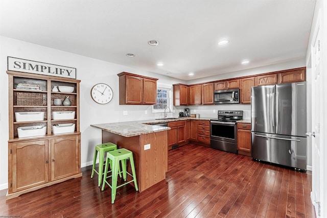 kitchen with dark wood finished floors, appliances with stainless steel finishes, a breakfast bar, a peninsula, and a sink