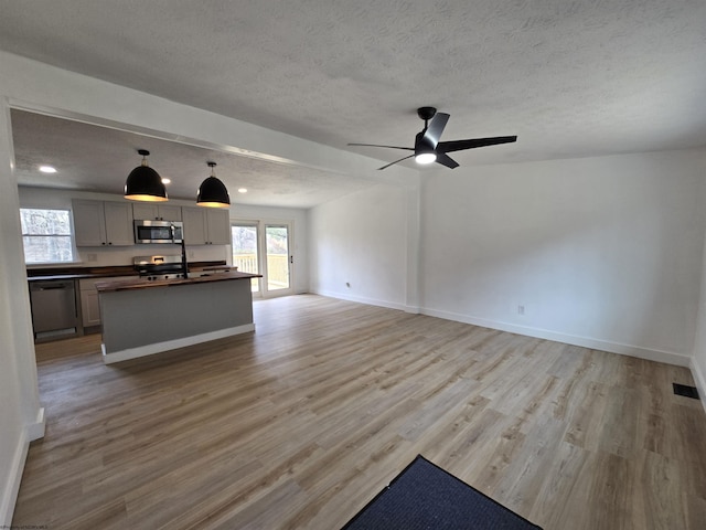 unfurnished living room with baseboards, a textured ceiling, and light wood finished floors