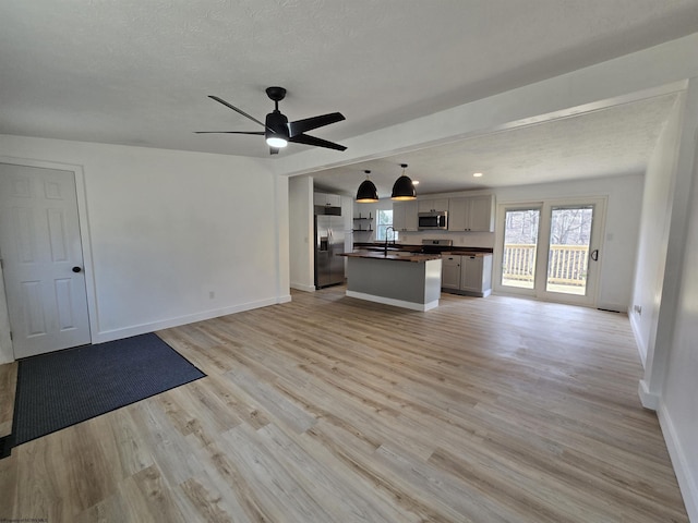 unfurnished living room with baseboards, ceiling fan, a textured ceiling, light wood-type flooring, and a sink